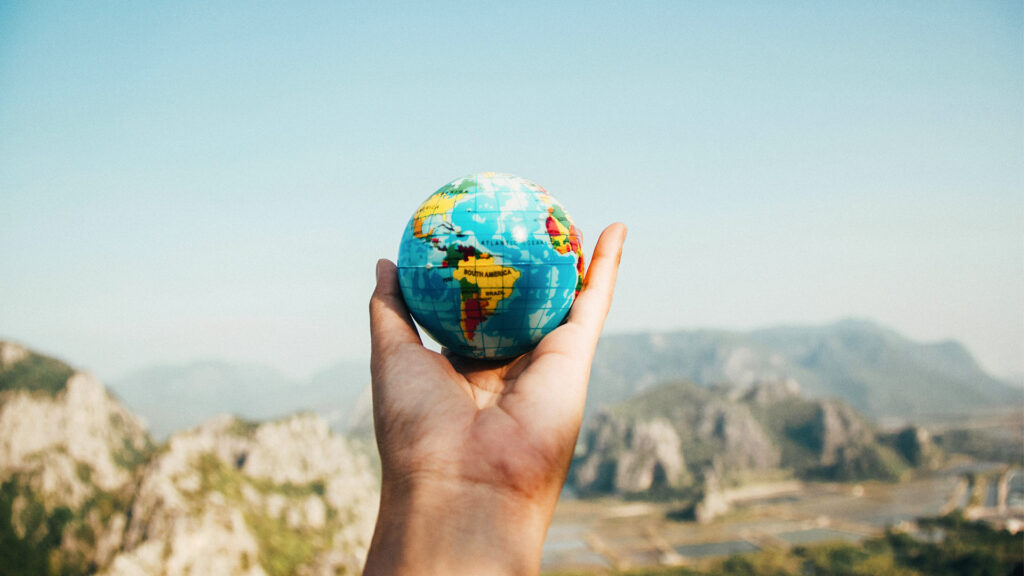 Person holding the globe in front of the mountain